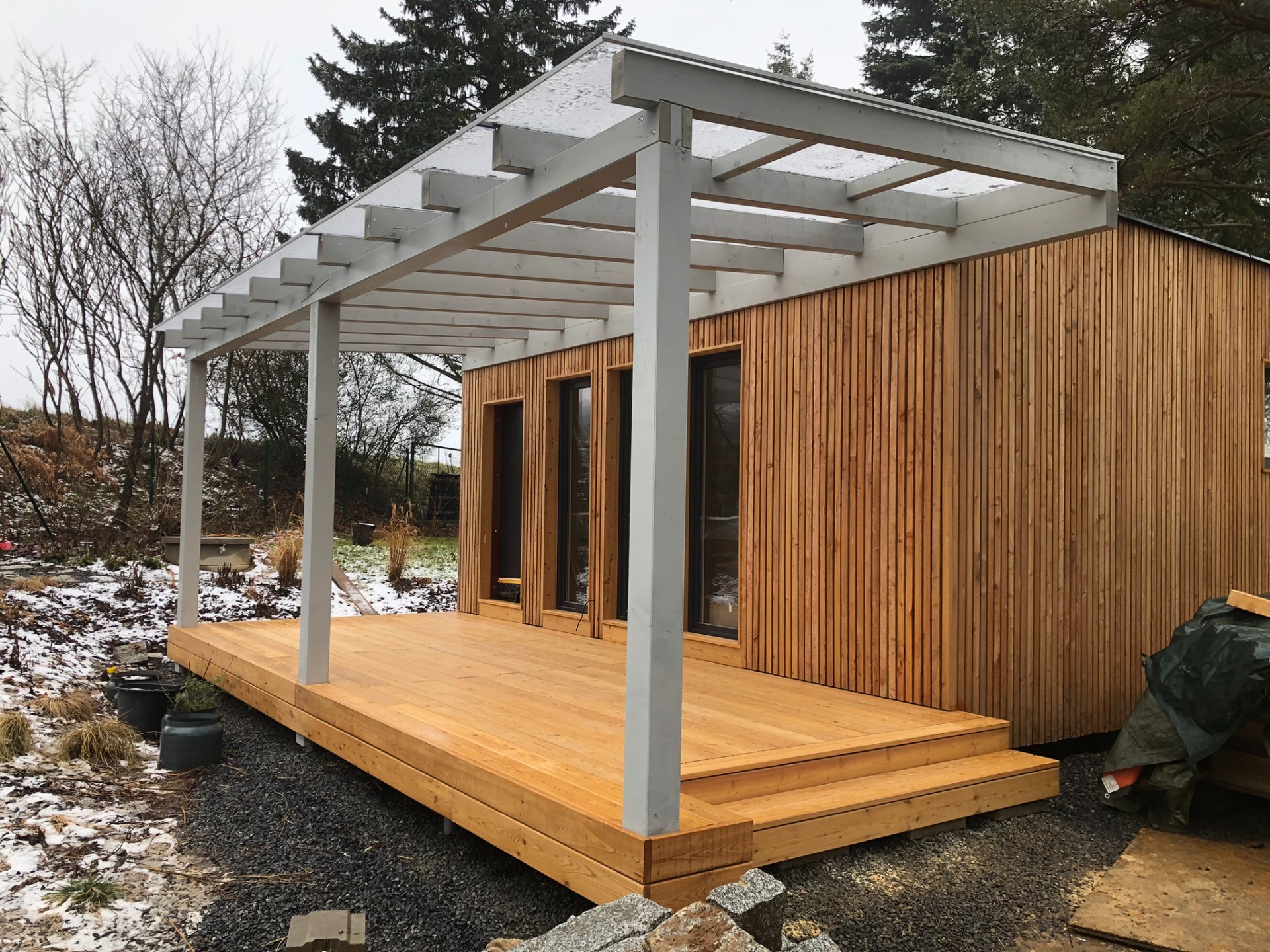 Dřevěná pergola s plným polykarbonátem nad dřevěnou terasou.